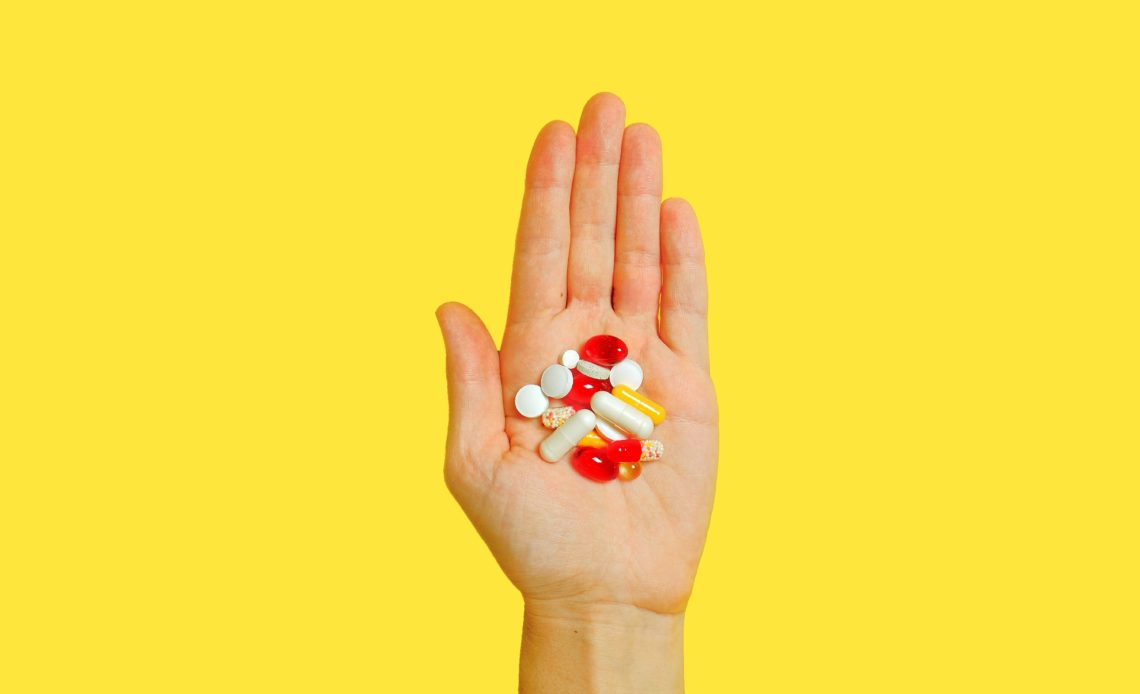 person holding a bunch of pills in the palm of their hand