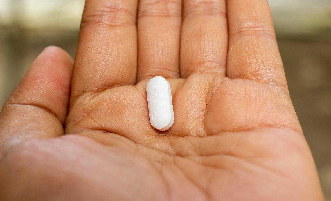 man holding white pill in palm of hand
