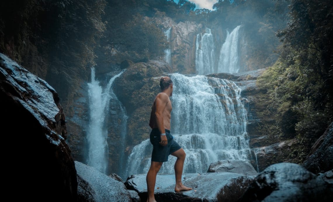 shirtless man standing by waterfall