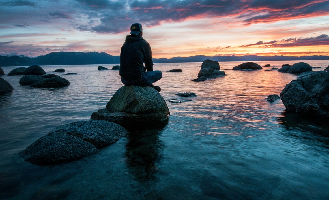 young man sitting on rock in water at dawn