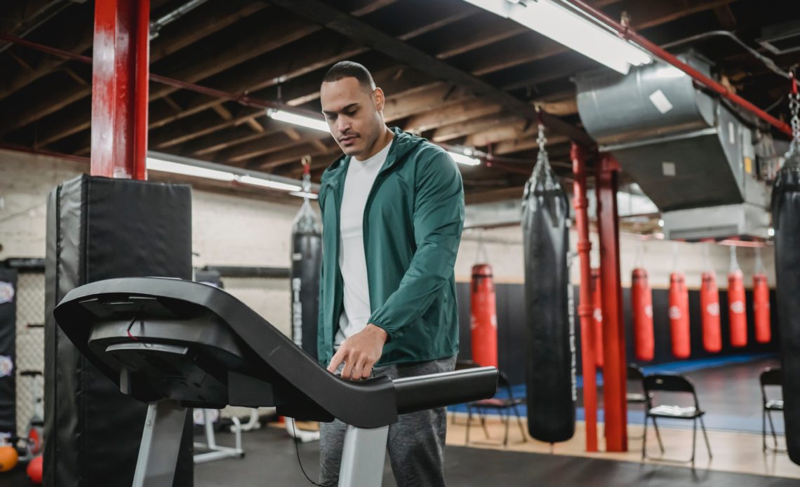 man in sweatshirt changing speed on treadmill at gym
