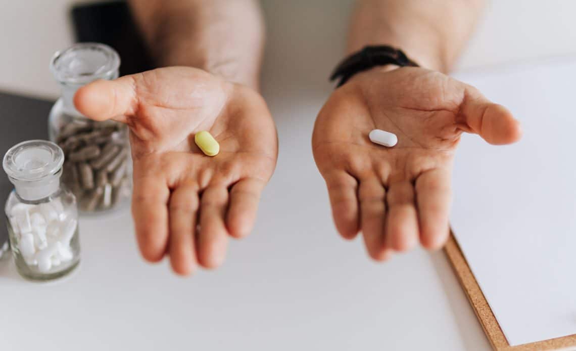 man holding yellow pill in right hand and white pill in left hand
